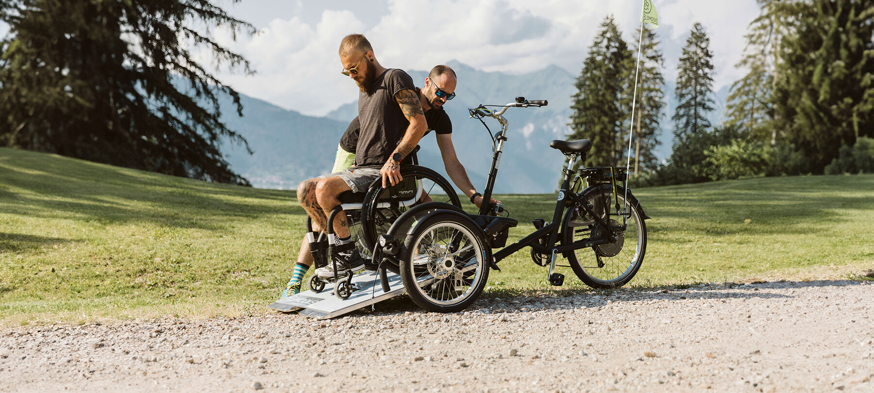 Ein junger Mann im Rollstuhl hat soeben den Konzertort erreicht und steigt von seinem Rollstuhlfahrrad ab, mit dem er vom Parkplatz zum Veranstaltungsort gefahren ist. Eine Person aus dem Remoove-Team hilft ihm und sorgt dafür, dass alles sicher abläuft.
