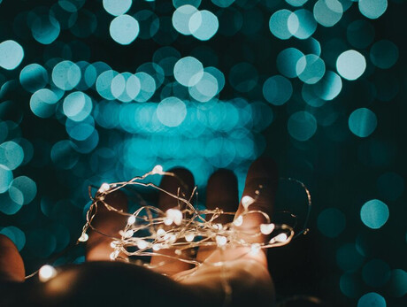 A hand holds a string of lights, with a dark background and blurred points of light creating a magical and evocative atmosphere