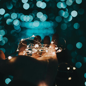 A hand holds a string of lights, with a dark background and blurred points of light creating a magical and evocative atmosphere