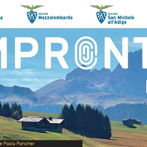 Paesaggio alpino con prati verdi, baite in legno e boschi ai piedi di una catena montuosa, immagine simbolo della rassegna culturale Impronte 2026