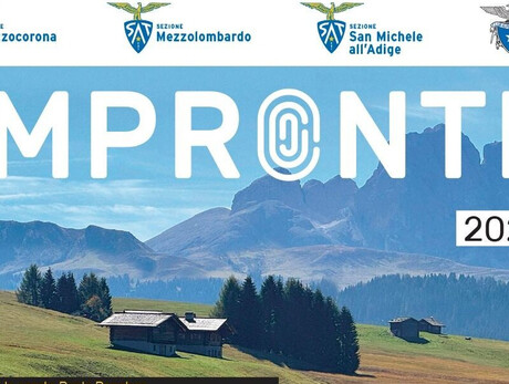 Paesaggio alpino con prati verdi, baite in legno e boschi ai piedi di una catena montuosa, immagine simbolo della rassegna culturale Impronte 2026