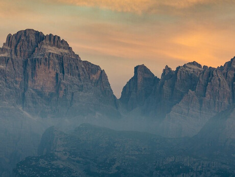L'immagine mostra le Dolomiti di Brenta all'alba e il cielo tinto di giallo-arancione