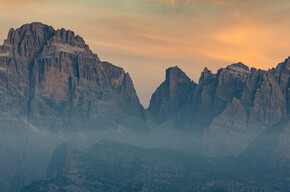 L'immagine mostra le Dolomiti di Brenta all'alba e il cielo tinto di giallo-arancione