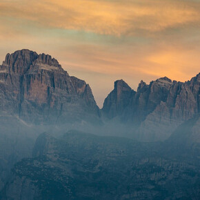 L'immagine mostra le Dolomiti di Brenta all'alba e il cielo tinto di giallo-arancione