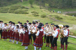 L'immagine mostra i componenti della banda con vestiti tradizionali mentre suonano all'aperto