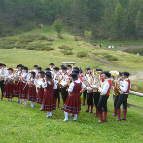 L'immagine mostra i componenti della banda con vestiti tradizionali mentre suonano all'aperto