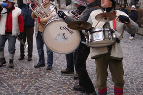 Nell'immagine si vedono i 5 componenti della banda intenti a suonare i loro strumenti in una piazza 