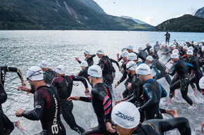 A group of X-Terra participants wearing wetsuits and swimming caps dive into Lake Molveno 
