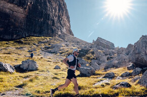The image shows an athlete from the Dolomiti di Brenta Trail with the Dolomites in the background