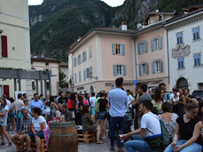 Persone che chiacchierano e degustano vino in piazza durante un evento estivo, tavoli con bottiglie e bicchieri.