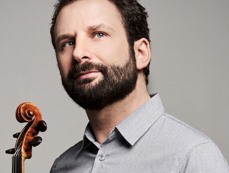 A man with a dark beard and micro-patterned gray shirt looks up towards the right against a gray background. At the bottom left, the neck and scroll of a violin are held near him.