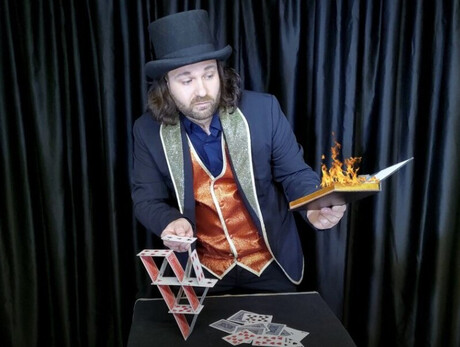 Magic Mister Mani Nella foto è presente Mr. Mani mentre è intento a costruire dei castelli di carte con una mano e reggere un libro infuocato nell'altra