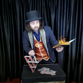 Nella foto è presente Mr. Mani mentre è intento a costruire dei castelli di carte con una mano e reggere un libro infuocato nell'altra