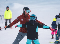 During an inclusive ski lesson on the snow of Paganella, an instructor helps a child find their balance on skis.