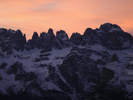 Nell'immagine si vedono le Dolomiti di Brenta innevate e il cielo che si tinge di rosa durante il tramonto