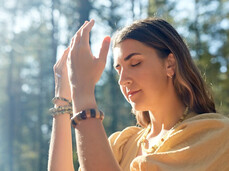The photo shows a girl in the woods absorbed in her connection with nature. Her eyes are closed, her hands are raised in mid-air and her face is serene.