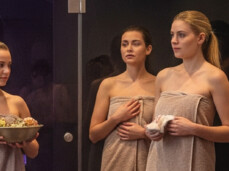 The photo shows a group of people inside a Turkish bath. A girl is holding a bowl with a scrub. The other people are waiting for the treatment.