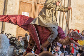 Ein Junge mit einer roten Mütze auf dem Kopf, der auf einem Marionetten-Dinosaurier reitet.