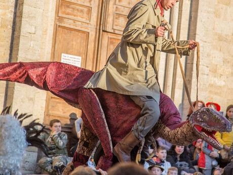 A boy wearing a red cap on his head riding a puppet dinosaur.