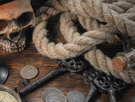 L'immagine mostra un tavolo con una mappa, una bussola, una corda e un teschio con una bandana dei pirati