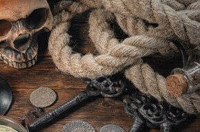 L'immagine mostra un tavolo con una mappa, una bussola, una corda e un teschio con una bandana dei pirati