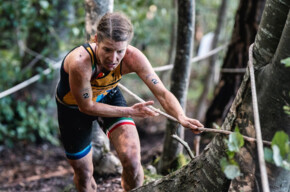 An X-Terra participant climbs up from a steep forest clinging to a rope.