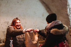 The photo shows the Christmas craft markets inside a vaulted passage in Faedo. In the center of the photo, there is a young woman who has bought something and is collecting her paper bag from the vendor.