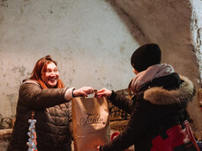 The photo shows the Christmas craft markets inside a vaulted passage in Faedo. In the center of the photo, there is a young woman who has bought something and is collecting her paper bag from the vendor.