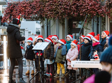 L'immagine mostra un coro di bambini vestito di rosso che cantano insieme melodie natalizie