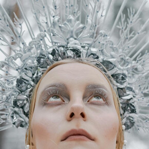  L'immagine raffigura la Regina delle Nevi, con un copricapo argentato ispirato al ghiaccio e un trucco etereo che richiama l'inverno. Lo sfondo naturale innevato enfatizza l'atmosfera magica e invernale.