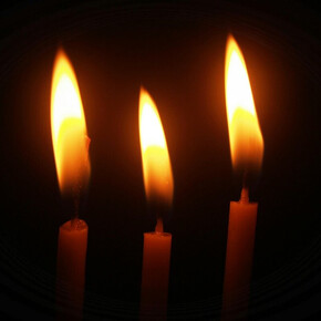 Tre candele accese su sfondo nero, con fiamme alte e luminose che brillano nell'oscurità.