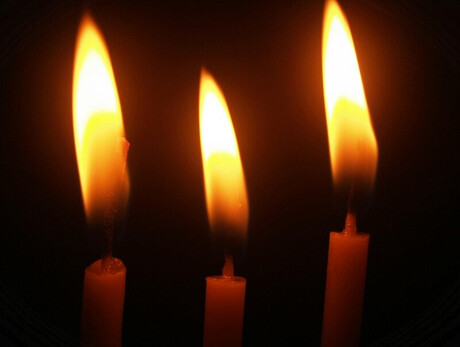 Tre candele accese su sfondo nero, con fiamme alte e luminose che brillano nell'oscurità.