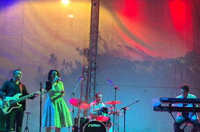 Three men playing instruments and one girl singing on stage with colorful lights
