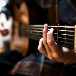 Primo piano della mano di un chitarrista che preme le corde sulla tastiera di una chitarra acustica durante l'evento.
