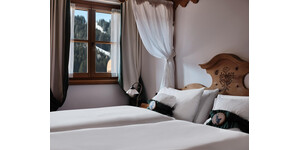 Una camera da letto accogliente con due letti singoli e lenzuola bianche. La finestra offre una vista sulle montagne innevate.